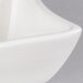 A close-up of an American Metalcraft white porcelain Squavy condiment cup with a curved edge.