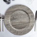 A dark gray faux wood melamine charger plate with silverware and a glass on it.