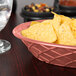 An oval paprika polyethylene basket filled with chips on a table next to a glass of water.