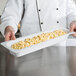 A chef holding a GET white melamine food pan of macaroni and cheese.