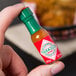 A hand holding a TABASCO® mini bottle of hot sauce.