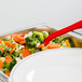 A red Cambro Camwear perforated salad bar spoon in a bowl of vegetables.