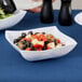A close up of a white Fineline plastic serving bowl filled with salad, olives, and black olives.