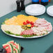 A white oval Carlisle melamine catering platter of cheese, meat, and fruit on a table.