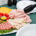 A white Carlisle melamine oval platter with meat, cheese, and other food items on a table.