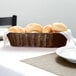 A Tablecraft brown rattan bread basket with rolls on a table.