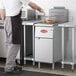 A man using an Avantco natural gas stainless steel floor fryer to cook food in a commercial kitchen.
