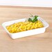 A white rectangular Pactiv Newspring microwavable container with yellow corn and parsley on a wooden surface.