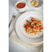 A Tuxton eggshell china bowl with a berry band filled with shrimp and rice with tomatoes and lemon.