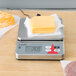 A Taylor digital portion scale on a counter with cheese on top.