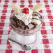 A Libbey Supreme Glass bowl filled with a banana split and chocolate sundae toppings with a spoon on a napkin.