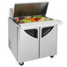 A Turbo Air stainless steel refrigerated sandwich prep table with food trays of vegetables and food.