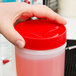 A hand holding a Carlisle white plastic container with a red spout and cap filled with pink liquid.