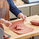 A person in gloves wrapping a piece of meat in pink butcher paper on a table.