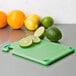 A San Jamar green bar size cutting board with limes and lemons on it.