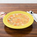 A yellow Fiesta china rim soup bowl filled with soup on a table.
