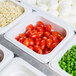 A white Cambro food pan with corn, peas, and green beans on a salad bar counter.