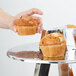 A hand holding a muffin on an American Metalcraft 3 tier display stand.