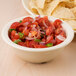 A Carlisle tan melamine nappie bowl filled with salsa and chips on a counter.