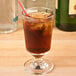 A Libbey footed highball glass filled with iced coffee and a straw.