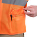 A close-up of a hand buttoning a pocket on an orange Cordova surveyor's safety vest.