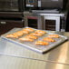 A Vollrath footed stainless steel cooling rack holding a tray of food.