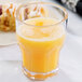 A close-up of a Carlisle clear plastic tumbler full of orange juice on a table.