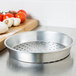 An American Metalcraft heavy weight aluminum pizza pan with holes on it sitting on a counter next to tomatoes.