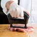A person in white gloves is using a Chef Master meat tenderizer on a piece of meat on a counter.
