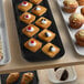 A black Cambro market tray of pastries and muffins on a counter.