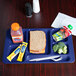 A navy blue Cambro 6 compartment tray with a sandwich, drink, and fruit on it.
