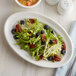 A Tuxton white oval china platter with a salad of lettuce, blueberries, and pecans.
