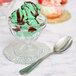 A Libbey glass bowl with green ice cream and chocolate syrup with a spoon on a plate.