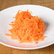 A plate of shredded carrots on a white table with a Robot Coupe 1/4" grating / shredding disc.