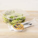 A clear plastic Genpak deli container of salad with a high dome lid and a fork.