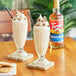 Two glasses of milkshakes with whipped cream and chocolate chips made with Torani Peanut Butter Flavoring Syrup.