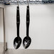 Two black Cambro salad bar spoons hanging from a metal rack.