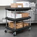 A black Metro utility cart with three shelves holding boxes.
