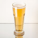A Libbey footed pilsner glass of beer on a table.