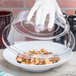 A gloved hand using a Carlisle clear polycarbonate lid to cover a bowl of pasta.