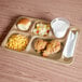A beige Cambro compartment tray with food and a glass of milk on a table.