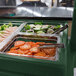 A green Cambro buffet / salad bar with trays of tomatoes and vegetables.