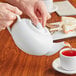 A person pouring tea into a white Acopa teapot.