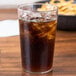 A clear Cambro polycarbonate tumbler of ice tea with ice on a table with a bowl of fries.
