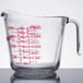 A clear glass Anchor Hocking measuring cup with red writing on it and a red handle.