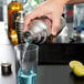 A person using a Vollrath stainless steel cobbler cocktail shaker to pour a drink.