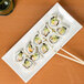 A CAC Tokyia bone white rectangular porcelain platter with sushi rolls on a table.