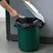 A hand putting a white plastic bag into a Rubbermaid green recycling can with a white lid.