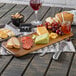 A Tablecraft acacia wood rectangular display board with cheese, crackers, and fruit on it.