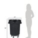 A woman standing next to a large black Rubbermaid trash can with wheels.